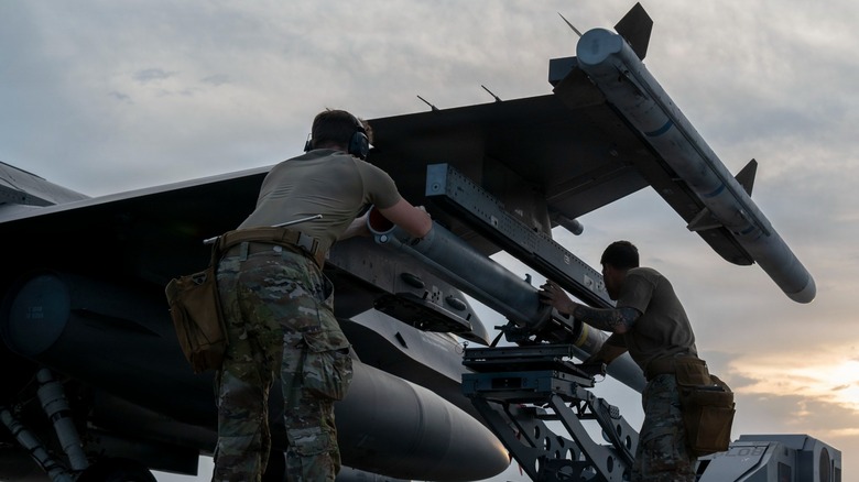 Airmen loading missiles onto an F-16 that holds an AIM-120 on its wingtip rail.