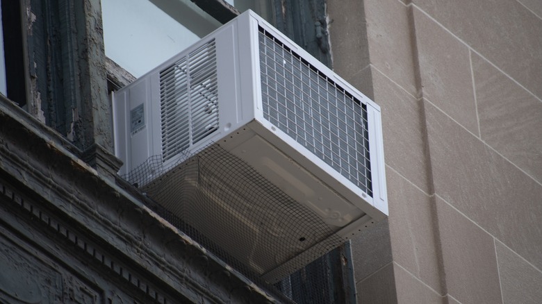 White window AC unit installed on a window in the top floor of a buiding
