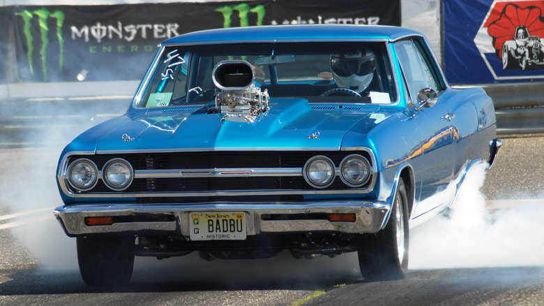 Modified 1965 Chevrolet Chevelle with Roots supercharger and open air scoop performing burnout during drag race staging
