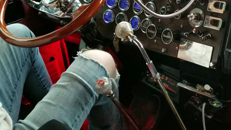 Close-up of twin shifters in a classic truck with a person sitting in the driver's seat.