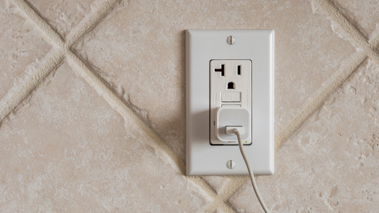 Charger plugged into a GFCI outlet on a tiled wall