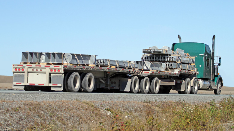 Gren semi truck carrying metallic beams driving down freeway