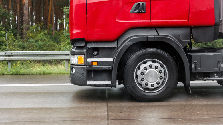 Close-up of a semi-truck front wheel driving on a wet highway