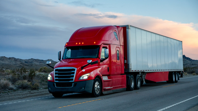 A red semi-truck hauling a white trailer at sunset
