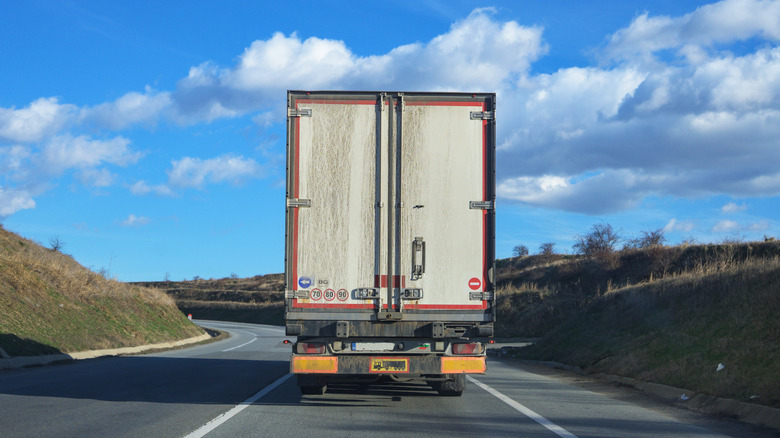 Rear view of a dirty truck with multiple stickers on a rural road.