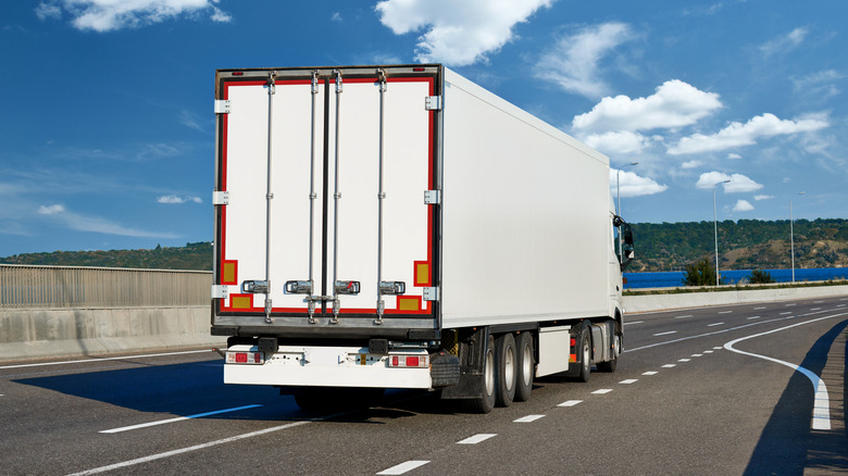 White semi-truck on a highway with reflective contour tape on the rear.