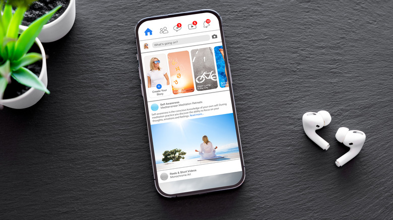 Facebook app open on a phone with a plant and airpods
