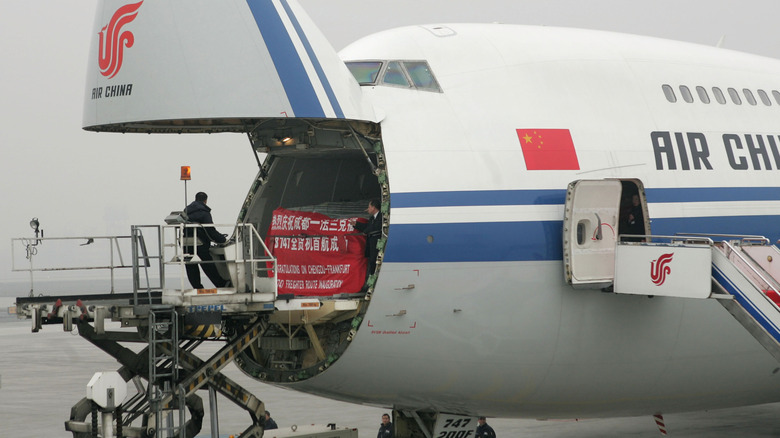 A worker loads freight through the open nose of a Boeing 747.