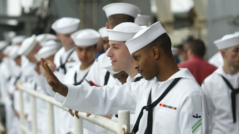 A group of sailors look out from the ship while performing "manning the rails" upon arriving home.
