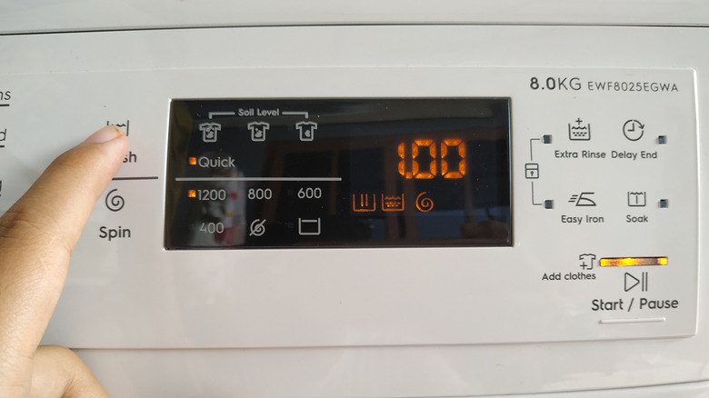 A woman's hand operating a washing machine's control panel