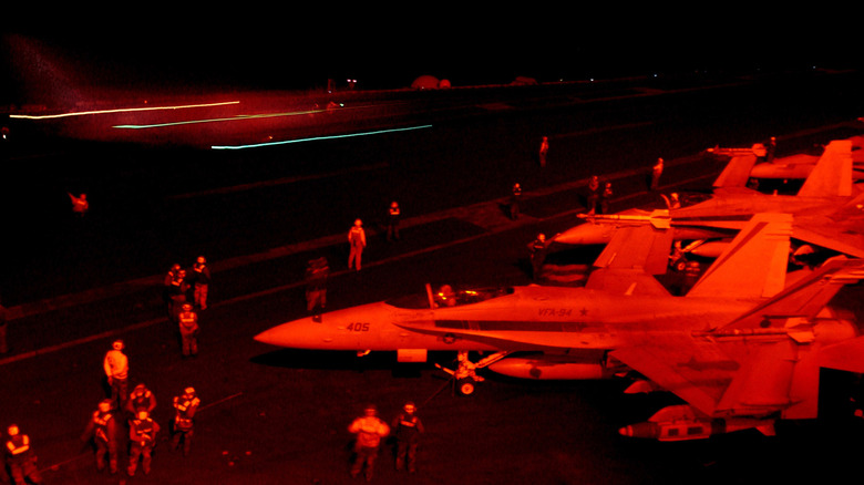 The flight deck of a U.S. Navy vessel at night illuminated with red lights