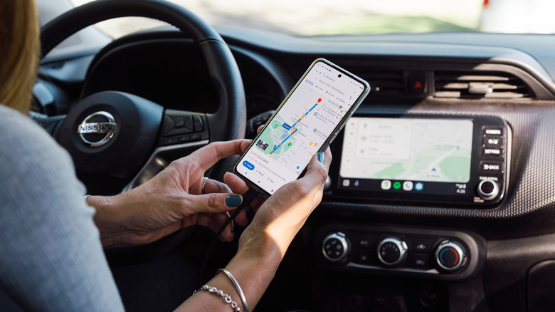 A person connecting an android phone running the Google Maps app to a car's head unit using a cable