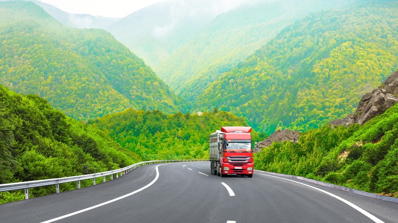 Semi-trailer truck driving on foggy, wooded mountain highway