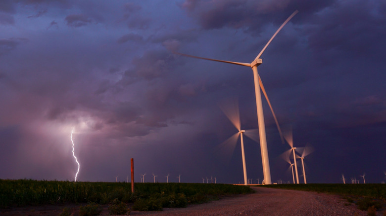 Low-angle shot of wind turbines during a storm, with a lightning bolt in the distance
