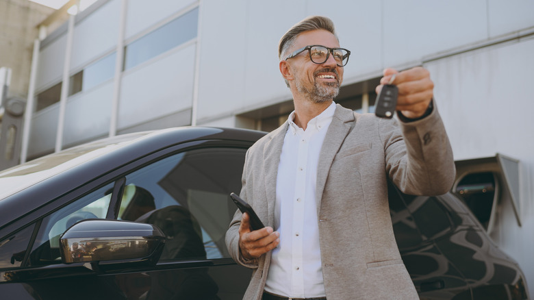 Man holding key fob and standing next to car