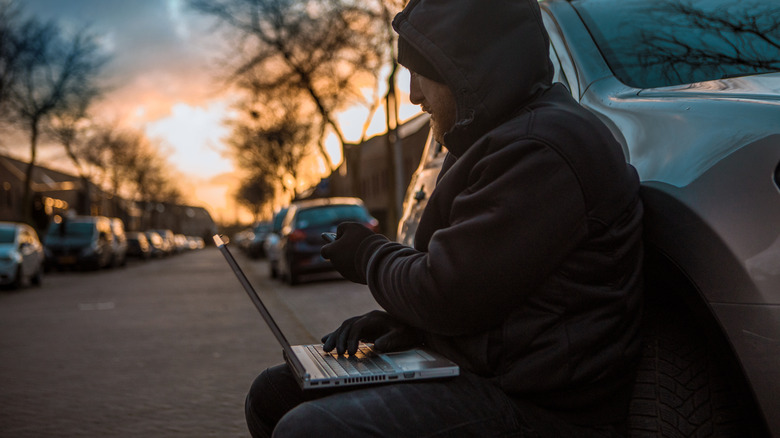 Car thief sitting outside car with laptop