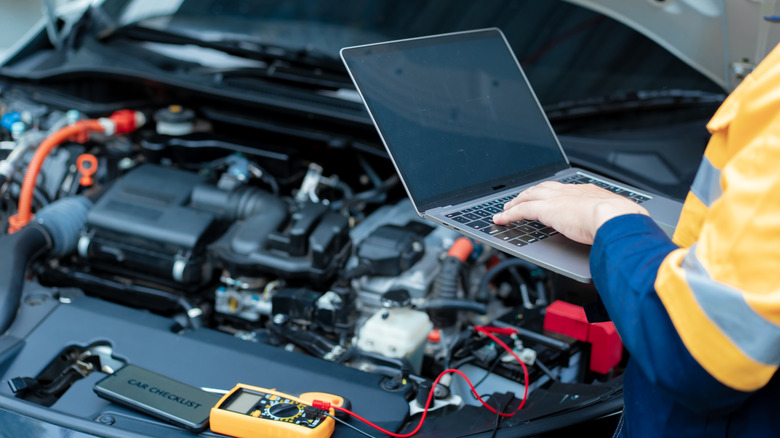 Mechanic holding laptop over engine bay