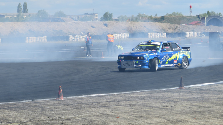 A blue BMW competitively racing and drifting around a turn on a closed race track.