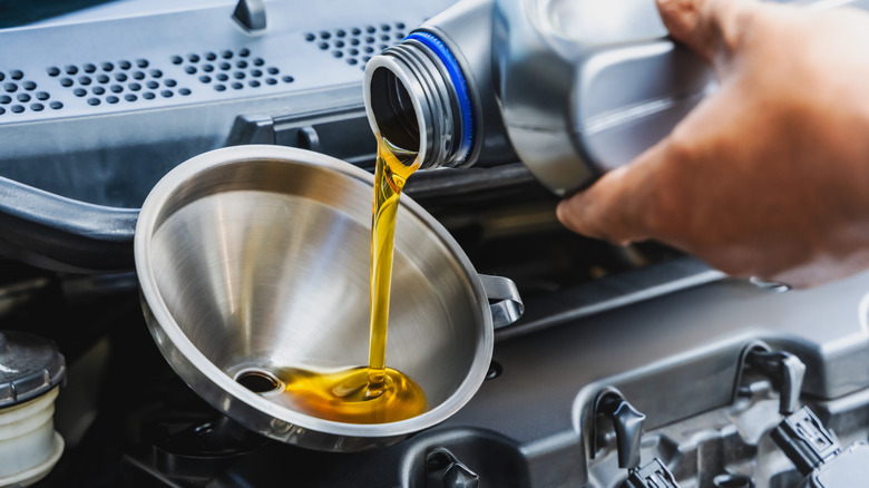 Hand pours engine oil into a funnel in the car
