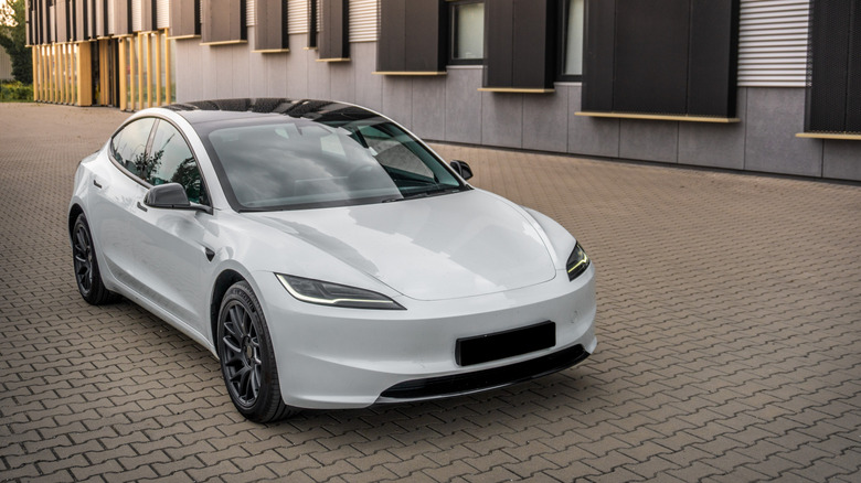 White Tesla Model 3 parked near a building on cobblestone pavement, front 3/4 view