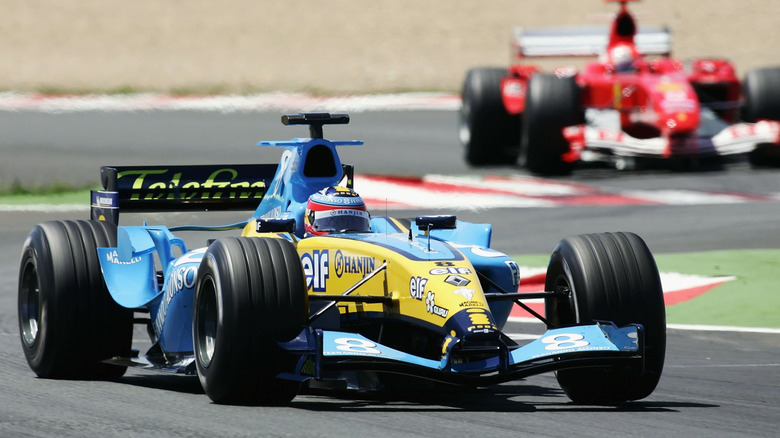 A yellow V-10-powered Renault R24 racing on a circuit, with a red F1 car trailing behind it.