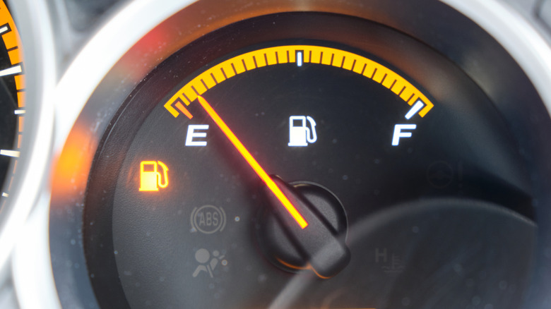 Close up of a car's fuel gauge with the needle nearly at empty and the warning light on.