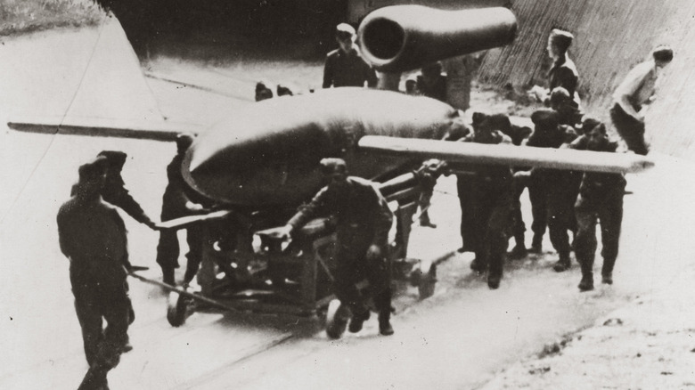 A V-1 flying bomb being wheeled out of a bunker on a railcar and inspected by Axis soldiers.