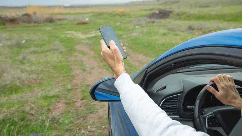 A man holding his smartphone up and out the window of a car in an attempt to get a signal