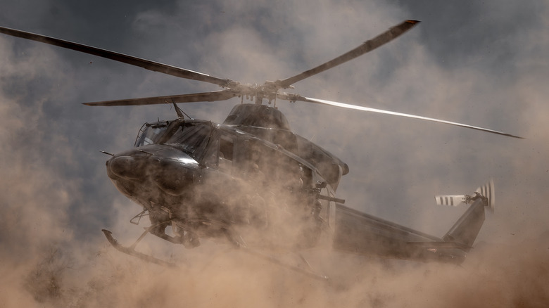 A military helicopter hovering and kicking up dust