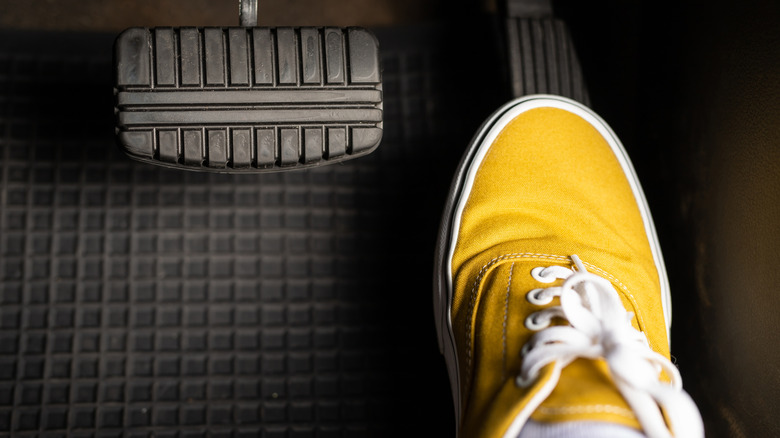 Foot in yellow sneaker presses on gas pedal