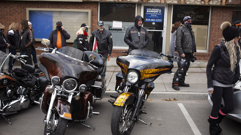 Parked motorcycles with people queuing behind them.