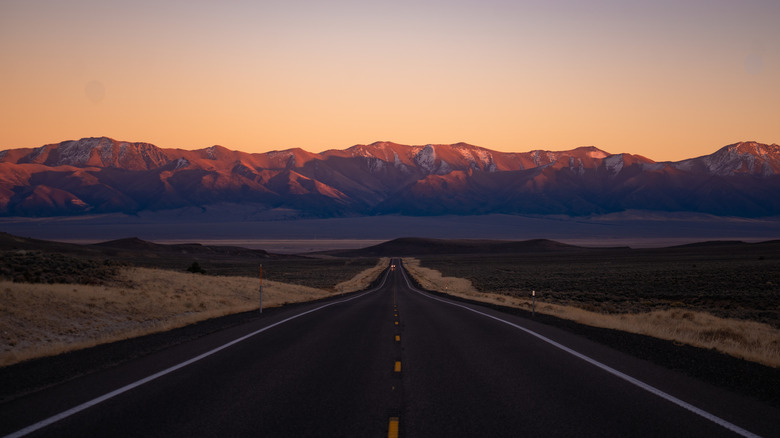 Sunset on a section of highway pointing towards scenic mountains.
