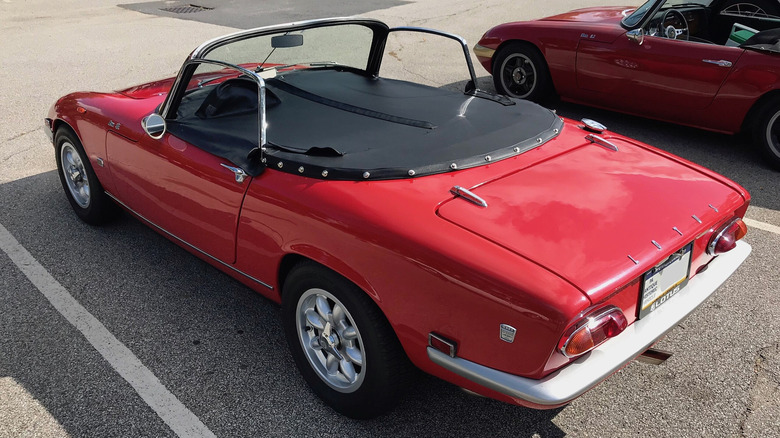 A left-hand drive red Lotus Elan S3 with tonneau cover fitted over the cabin, rear 3/4 view