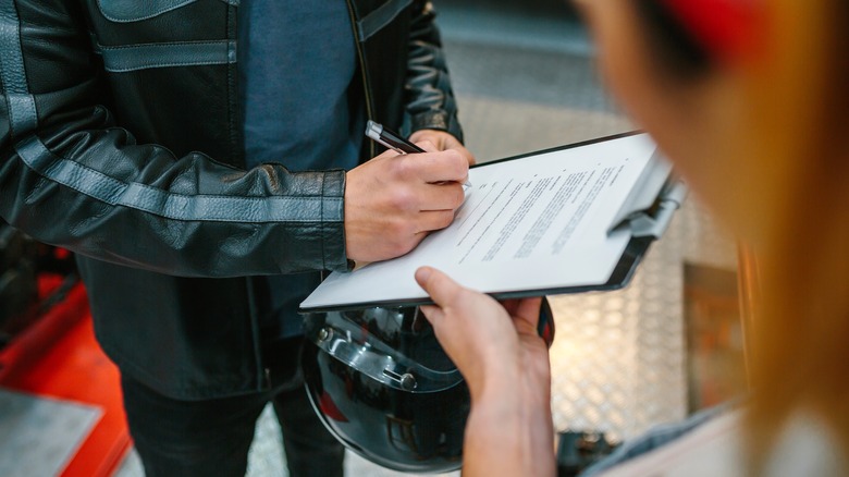 Unrecognizable biker man wearing leather jacket and holding helmet signing insurance policy