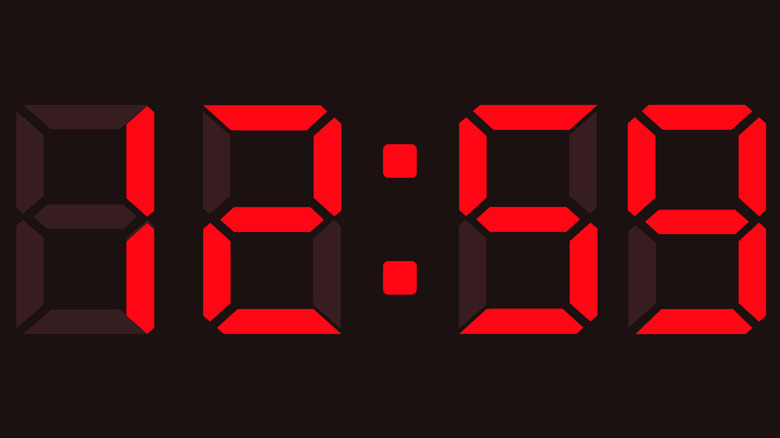 Close up of a digital clock face showing the time 12:59 in bright red LED