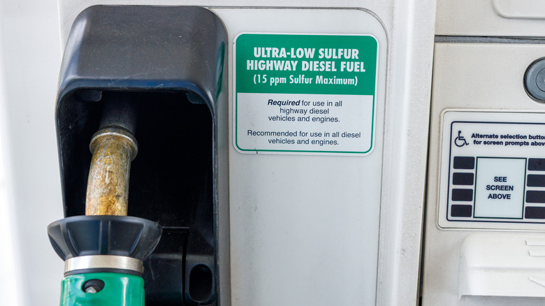 A worn diesel fuel nozzle rests in its holster beside a green ultra low sulfur highway diesel label