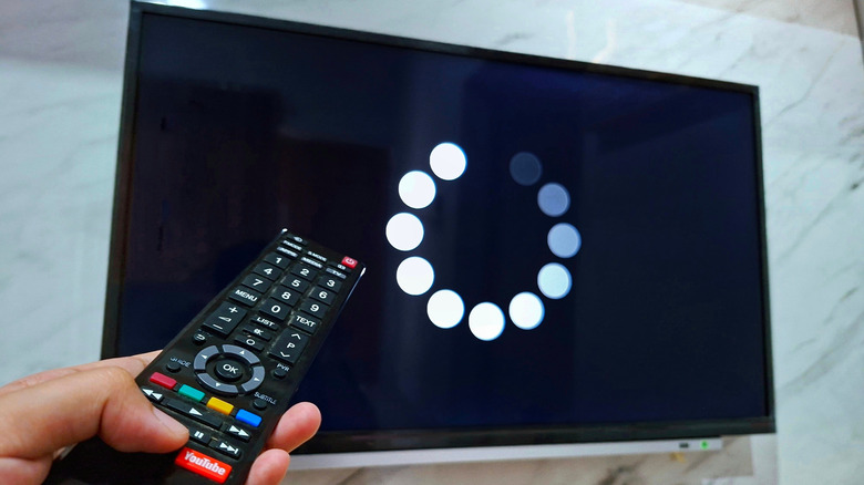 A person holding a remote with a buffering video in the TV
