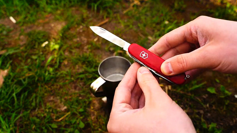 Man holding unsheated Swiss Army knife over metal cup