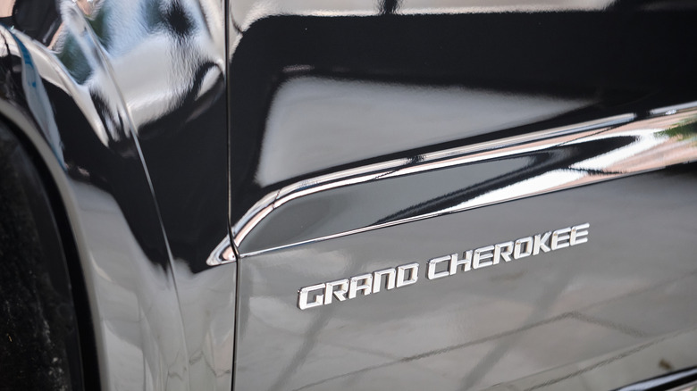 Image shows a reflective, black-painted door panel with a silver-colored 'Grand Cherokee' badge.