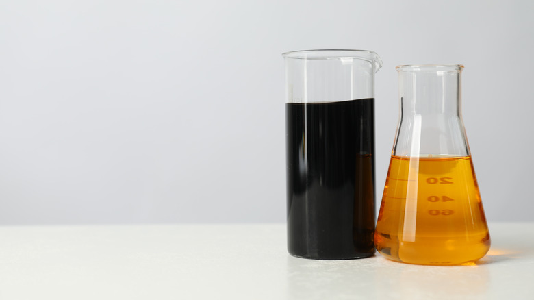 Two beakers on table with black and golden-brown oil in each