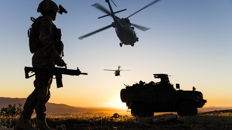Soldier with weapon on a field with helicopters and a tank