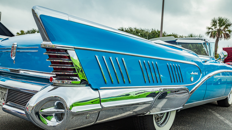A low-angle shot shows the highly stylized rear fin, bumper, and chrome work on a blue 1958 Buick.