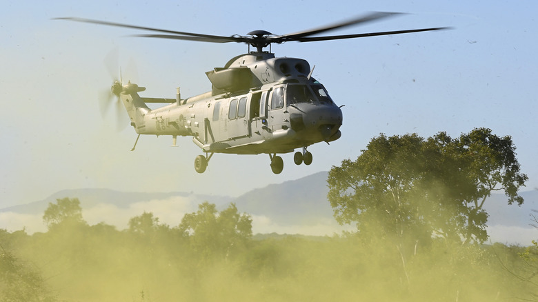 Military helicopter hovering in a grassy field