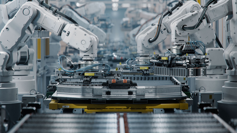 Row of White Robotic Arms at Modern Factory. Lithium-Ion EV Battery Pack Production