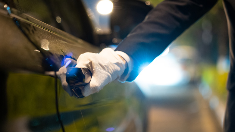A person with white gloves on trying to open a vehicle door at night.
