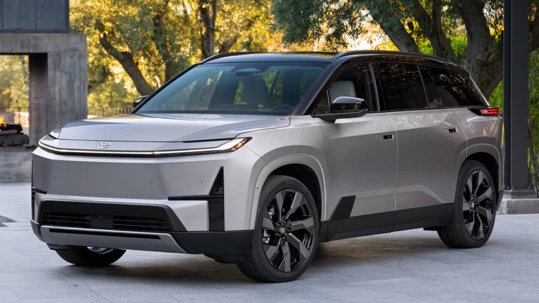 2027 Toyota Highlander EV parked with trees and a concrete structure in the background.