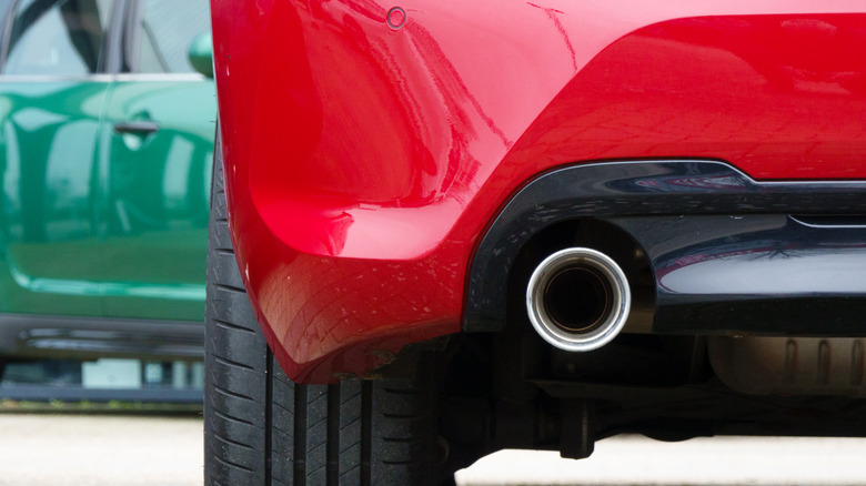 Close-up of a single exhaust pipe on a red car with a green car in the background