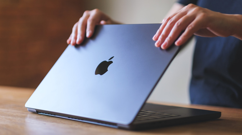 Person opening the lid of a Midnight colored MacBook