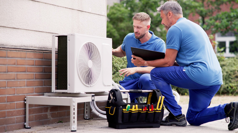 Two men installing an air conditioning unit outside a building