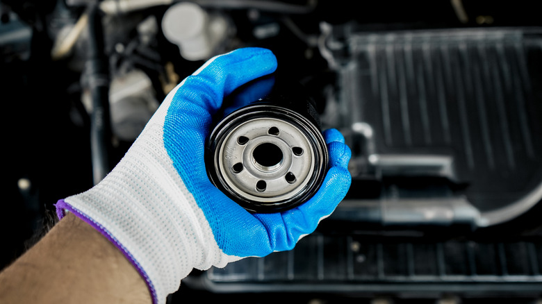 A gloved hand holding an oil filter